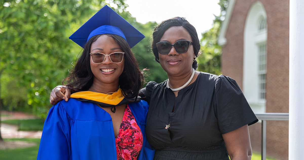 Oluebube Akujieze (left) wears her UD Commencement regalia while posing with her mother, who's wearing a black dress , on campus.