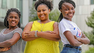3 women smiling with arms crossed in front of a building