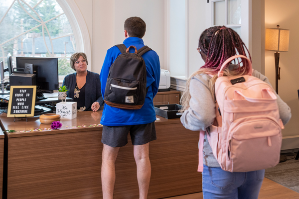 students speak with a receptionist at a desk in front of an arched window