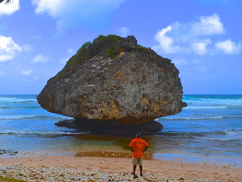 Man regarding giant rock structure on beach