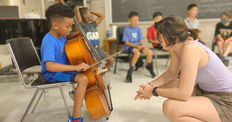 CMS Administrative Assistant and teacher Emme Whisner introduces a young student to the cello during Meet the Instruments camp. CMS Administrative Assistant and teacher Emme Whisner introduces a young student to the cello during Meet the Instruments camp.