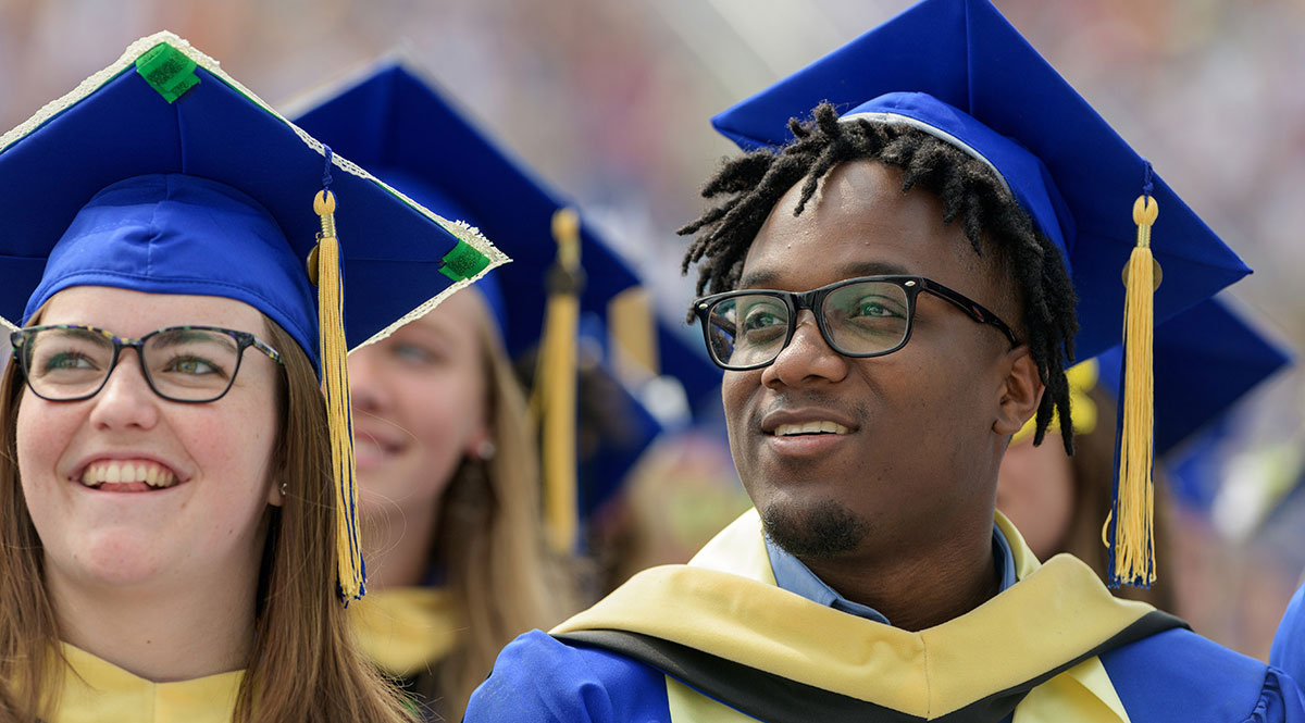 A male and female, dressed in blue robes, smile at their graduation from the University of Delaware.