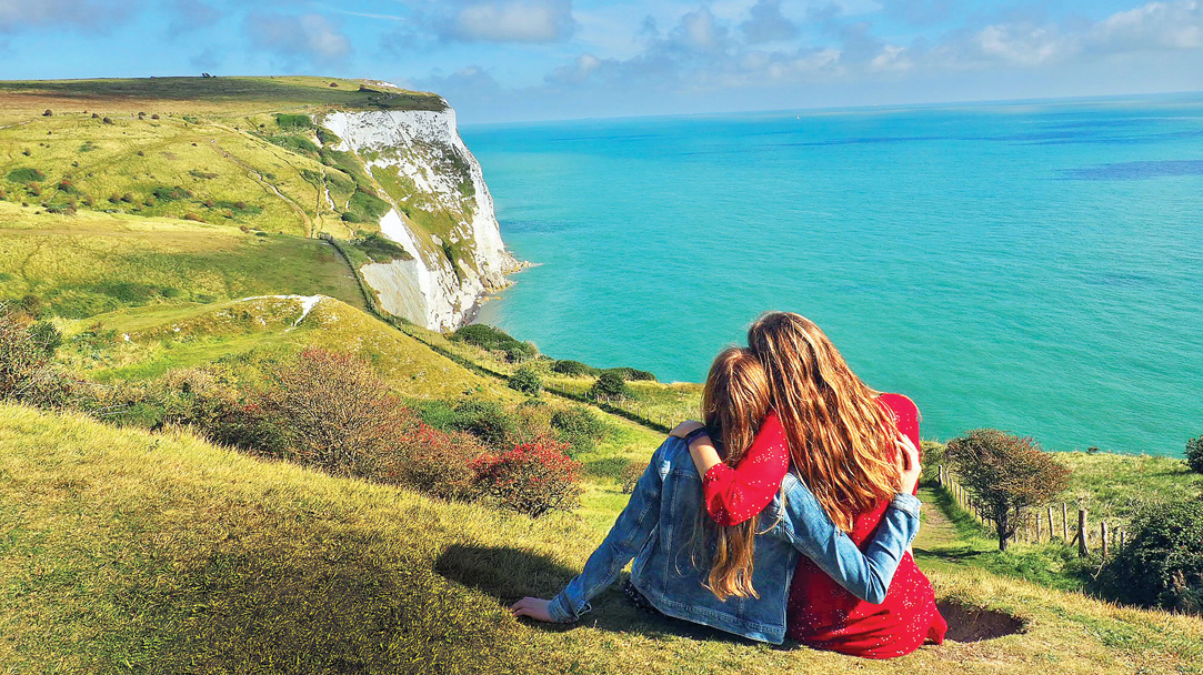 A couple of students sitting over a cliff that faces the ocean on a sunny day.