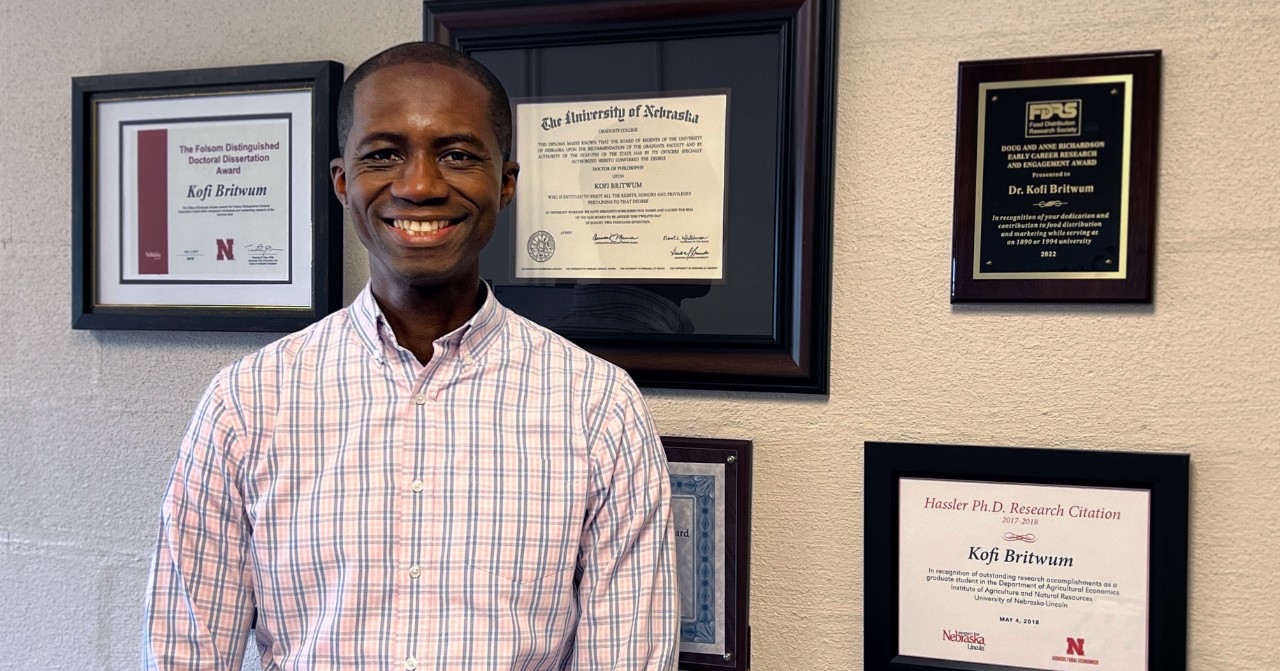 Meet our new faculty: Kofi Britwum Kofi Britwum stands in front of his awards and plaques.