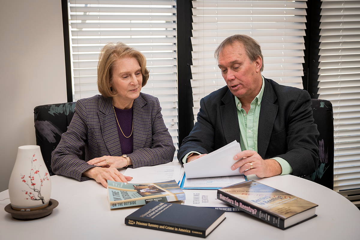 A man and woman, both UD faculty, sit at conference table and review books and articles related to Center for Drug and Health Studies research.