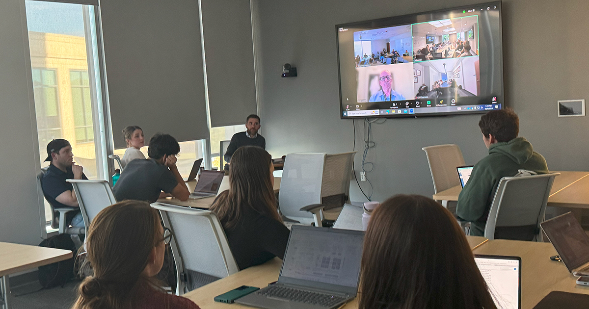 Students sit in a classroom around tables with their laptops out as they watch a Zoom presentation with aging expert Steven Austad of the University of Alabama Birmingham. Students in similar classes at Colorado State University and the University of Colorado Boulder have also Zoomed in to the discussion and are featured on the large TV screen at the front of the class.