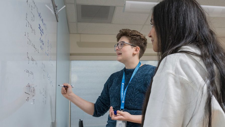 Female math instructor teaching female student at a white board