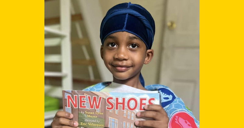 Young boy holds a book titled New Shoes