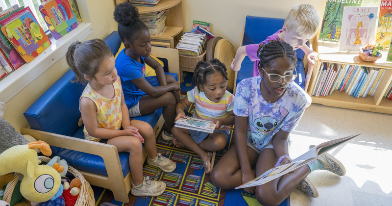 4 young children being read to by older child 