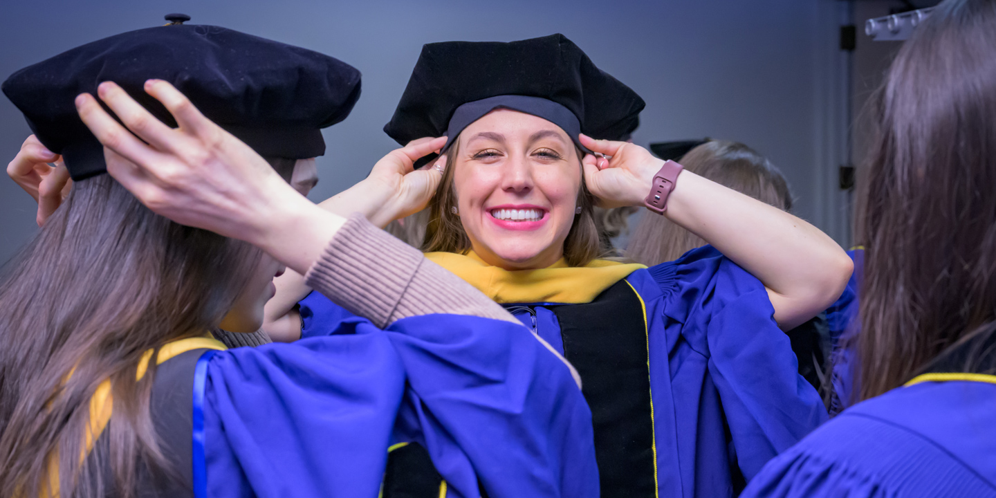 Student places cap on their head during the Doctoral Hooding Ceremony.