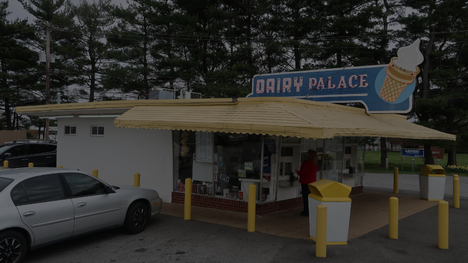 Wide shot exterior photo of the Dairy Palace ice cream shop pickup window, including the original fifties-style awning and ice cream cone-shaped neon sign