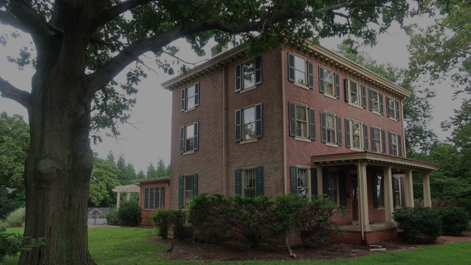 Exterior photo of a grand, historic brick home in Delaware including a view of a front porch and surrounding greenery