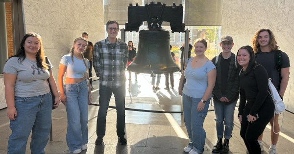 Six adults standing and smiling in front of the Liberty Bell in Philadelphia