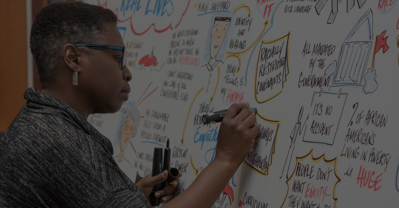 Photo of a woman writing public policy brainstorming ideas in colorful doodles on a large whiteboard.