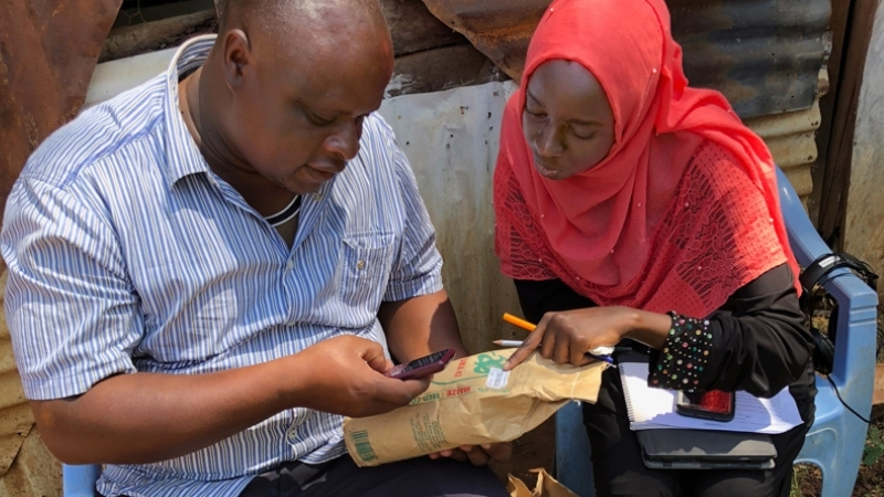 Mariam and a Kenyan farmer looking at a seed packet and his cell phone.