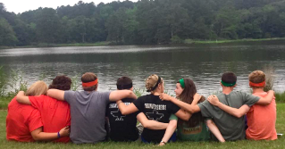 Kids sitting in a row in front of a large pond at camp