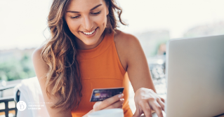 A woman on her laptop smiling while holding her credit card