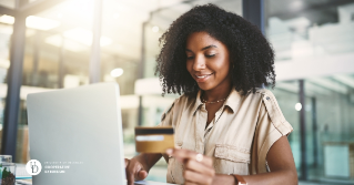 a woman smiling at her laptop while holding her credit card