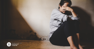 A photo of a mother sitting alone on the floor covering her face in distress