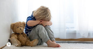 a small child on the floor with his head down in sadness next to his teddy bear