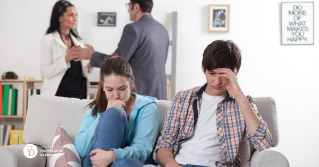 A husband and wife arguing while two teens worry on the couch