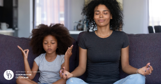 A mom meditating on the couch with her daughter