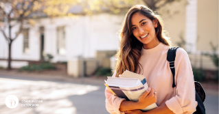 A female college student smiling while holding books on campus