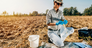 A woman taking a soil sample with a white bucket next to her in a field