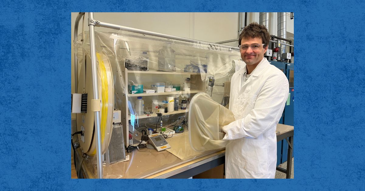 Christian Dewey stands with his hand in an anaerobic chamber, a bag that fills up with mostly nitrogen.