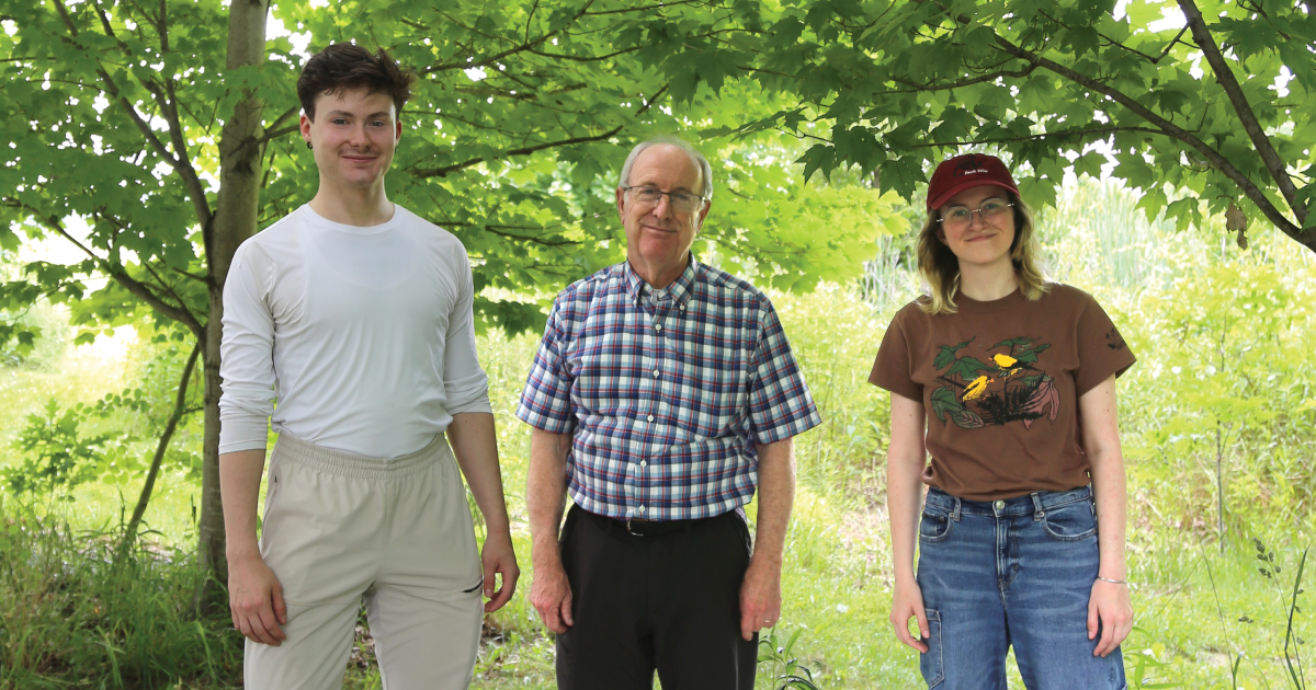 Doug Tallamy stands in a field with two students.