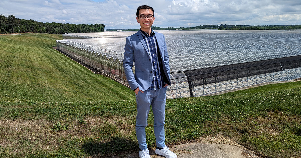 Qingwu Meng standing in front of a large commercial sgreenhouse.