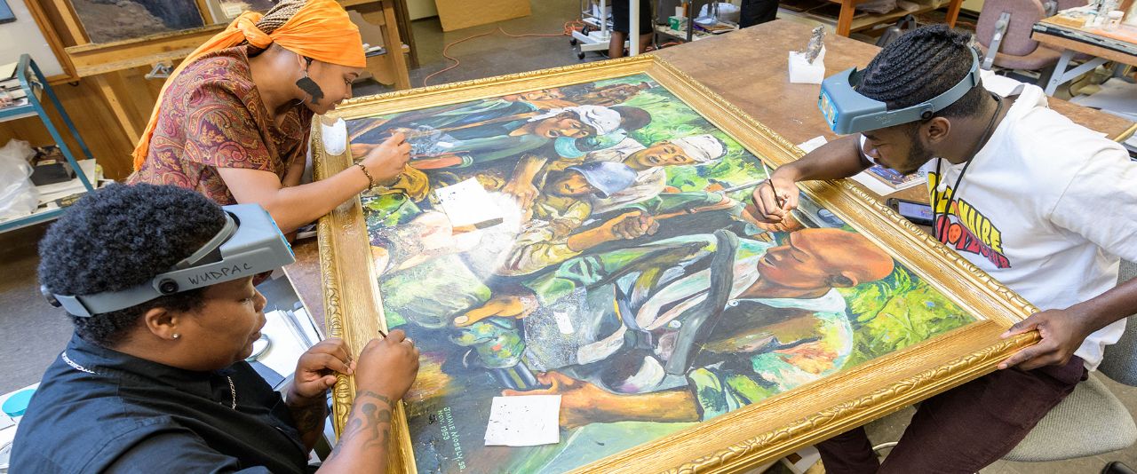 Three students cleaning up an old mural for Black History artwork