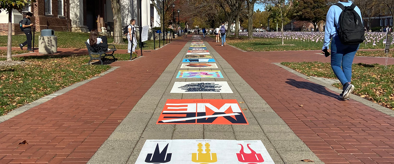 Colorful posters installed on a walkway of concrete pavers and red brick on a college campus.