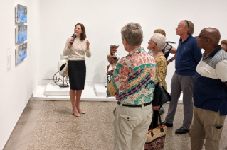 People standing in a museum looking at three blue horizontal pieces of artwork on a wall