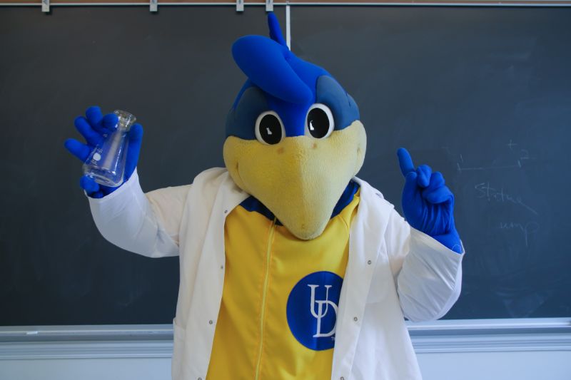 YouDee mascot in lab coat in front of chalkboard