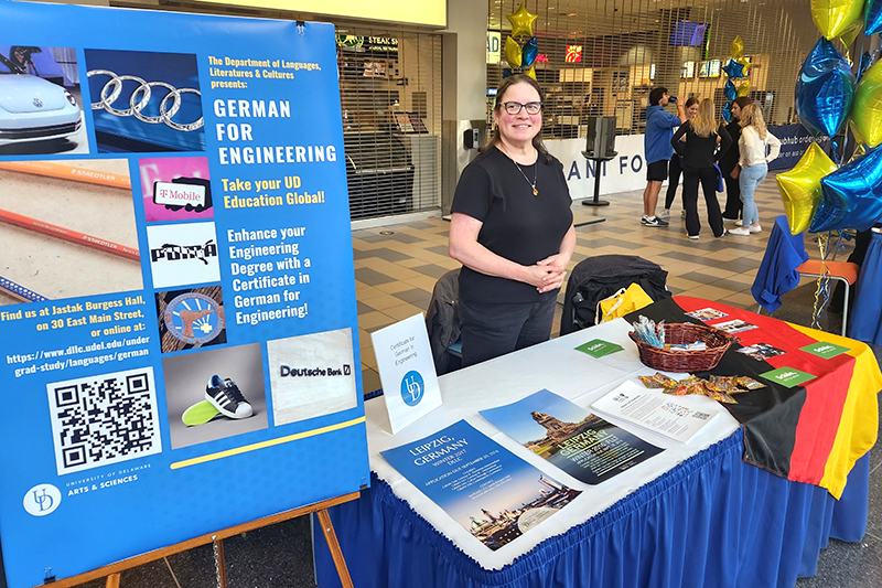 A staff person inside a university student center stands at a table with signs and brochures with information about an academic program.