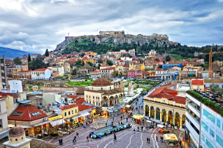 City of Athens, Greece, with the ancient ruins of the Acropolis on a hilltop overlooking a downtown area of stucco buildings with red tile roofs.