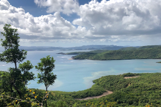 View on a sunny day of an ocean inlet surrounded by a lush green mountainous landscape.