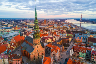 Aerial view of the historic town of Riga, Latvia, with a gothic church surrounded by medieval buildings, next to a river in the background.