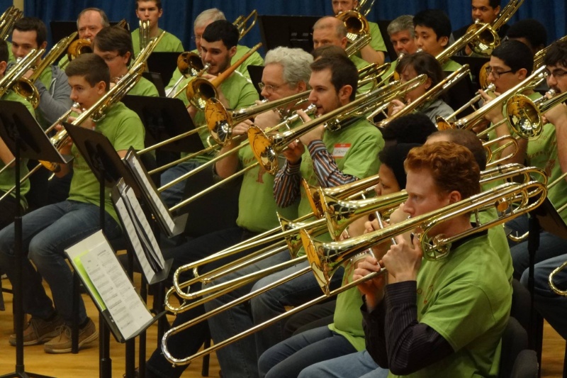 People seated playing trombones on stage in green shirts