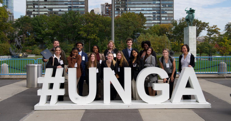 UD Students Study Abroad Trip April 2024 they stand behind a sign with haghtag UNGA for United Nations General Assembly