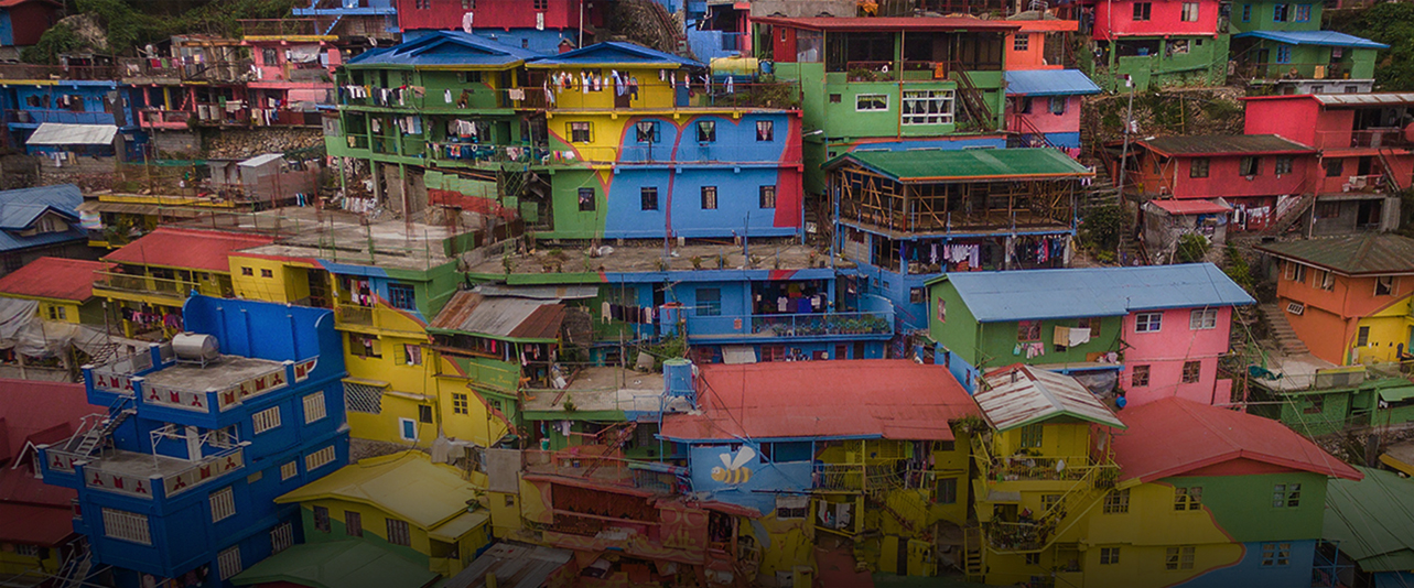 Colorful buildings, painted green, blue, yellow, red, and orange, are stacked closely together on a steep hillside.