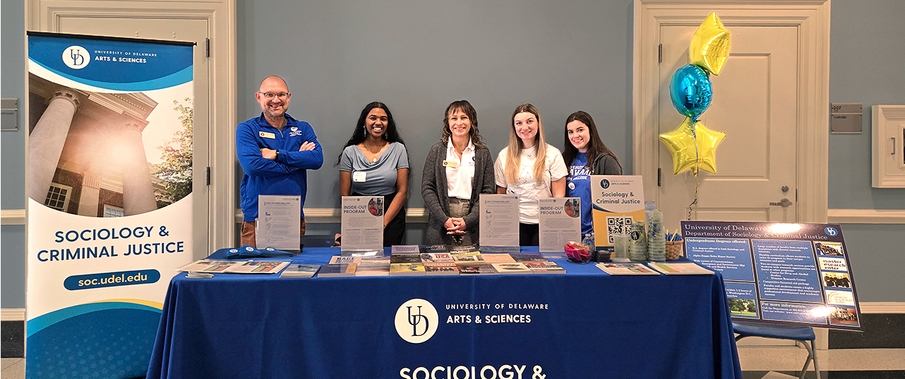 Blue and Golden table for sociology and criminal justice department with five people standing behind it