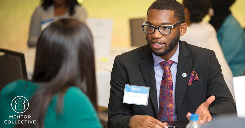 A young professional wearing a suit talks to a UD student during an event hosted by UD's Office of Development and Alumni Relations