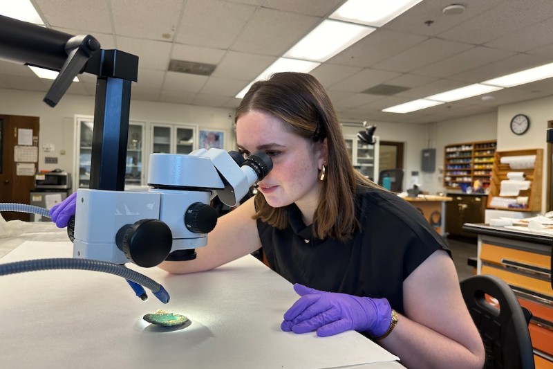  A student looks through a microscope at a small metal object illuminated by the microscope's light.