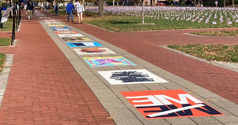 Colorful posters installed on a walkway of concrete pavers and red brick on a college campus.