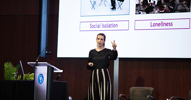 A University of Delaware presents her research while standing on a stage next to a podium with a slideshow on the screen behind her.