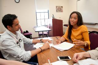 Two college students sitting at a desk working on course work inside a classroom.