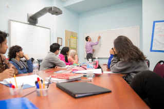 Group of adult international students at a conference table looking at a white board