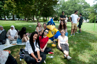 A group photo of about 12 international students with the YoUDee mascot on a lawn during a picnic.